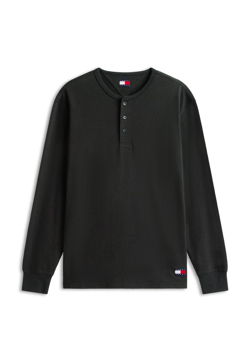 Schwarzes langärmliges Waffelstrickshirt mit drei Knöpfen am Kragen und kleinen Tommy Jeans Logo-Patches auf Brust und unterem Saum.