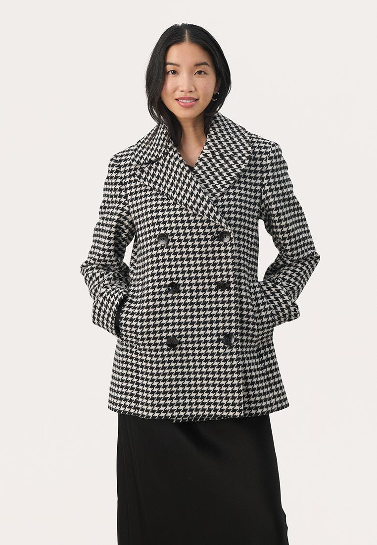 Schwarz-weißer Peacoat im Hahnentritt-Muster mit einem breiten Kragen, doppelreihigen Knöpfen und seitlichen Taschen, kombiniert mit einem schwarzen Rock.