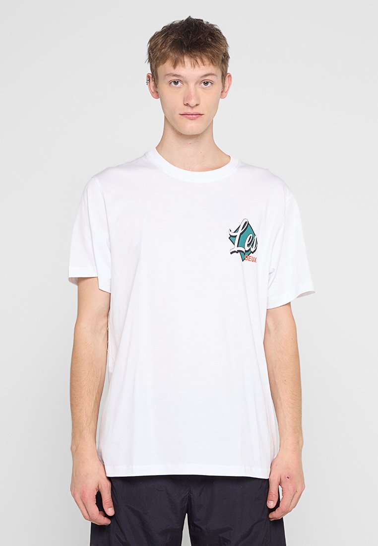 Weißes Baumwoll-T-Shirt mit lockerer Passform, das ein bedrucktes Logo in Grün und Rot auf der linken Brustseite zeigt. Kurze Ärmel, Rundhalsausschnitt.