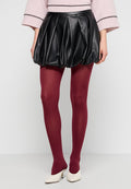 Schwarzer, plissierter Leder-Bubble-Rock mit burgunderroten Strumpfhosen und weißen High Heels, getragen mit einem hellrosa Pullover.
