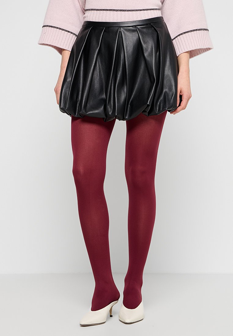 Schwarzer, plissierter Leder-Bubble-Rock mit burgunderroten Strumpfhosen und weißen High Heels, getragen mit einem hellrosa Pullover.