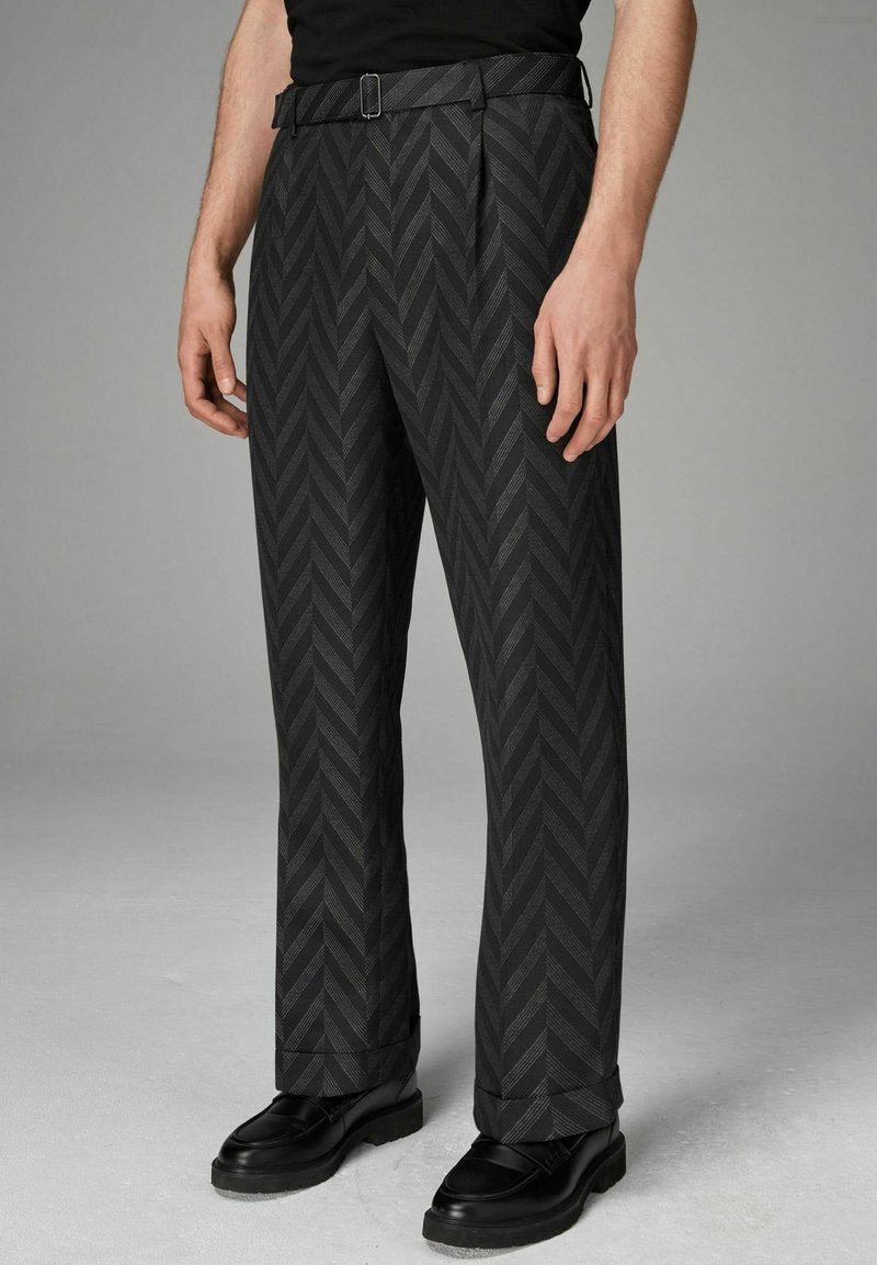 Schwarze Hosen mit einem Fischgrätmuster, geradem Schnitt und einem Gürtel mit einer Metallschnalle. Tragen mit schwarzen Schuhen, die die Textur und das Design hervorheben.