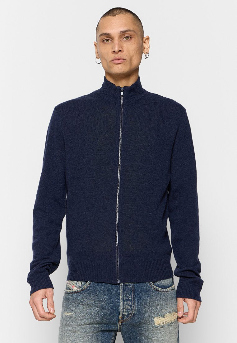 Navy Zip-Up-Pullover mit hohem Kragen, gerippten Ärmelbündchen und Saum, glatte Textur, aus weichem Strickmaterial, getragen über ausgewaschenen blauen Jeans.