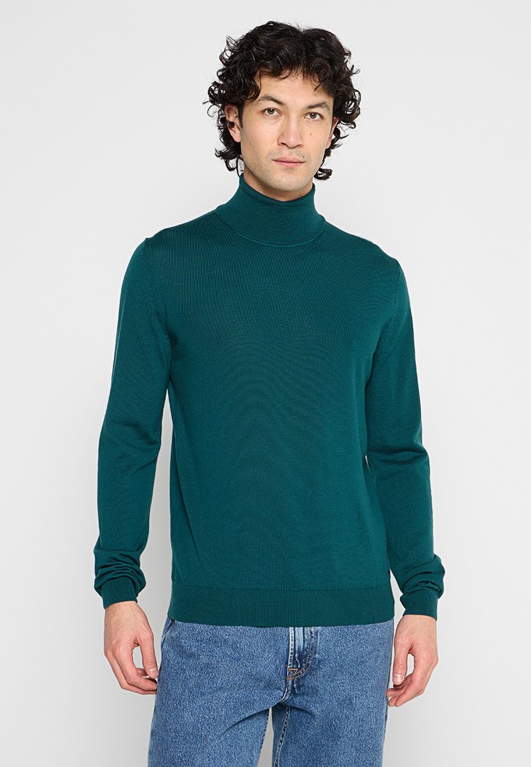 Dunkelblauer Rollkragenpullover mit gerippter Textur, tailliertem Schnitt und langen Ärmeln. Kombiniert mit hellblauen Jeans.