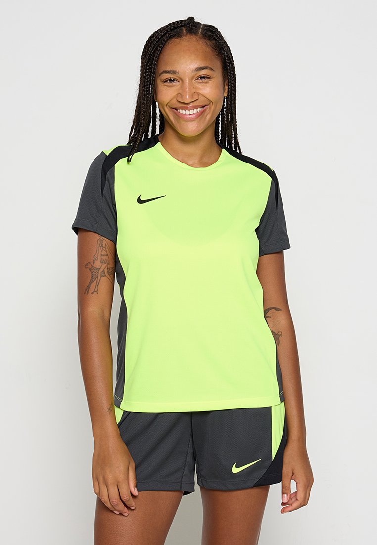 Neon-gelbes, kurzärmeliges Sportshirt mit schwarzen Akzenten, kombiniert mit dunklen Shorts mit kleinem Logo, aus atmungsaktivem Material.