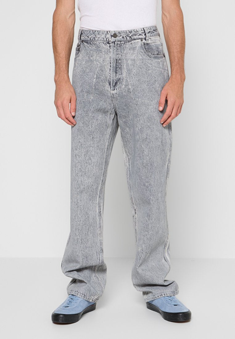 Frontansicht einer Person, die hellgraue Acid-Wash-Jeans, ein weißes Tanktop und hellblaue Sneakers mit schwarzer Sohle trägt.