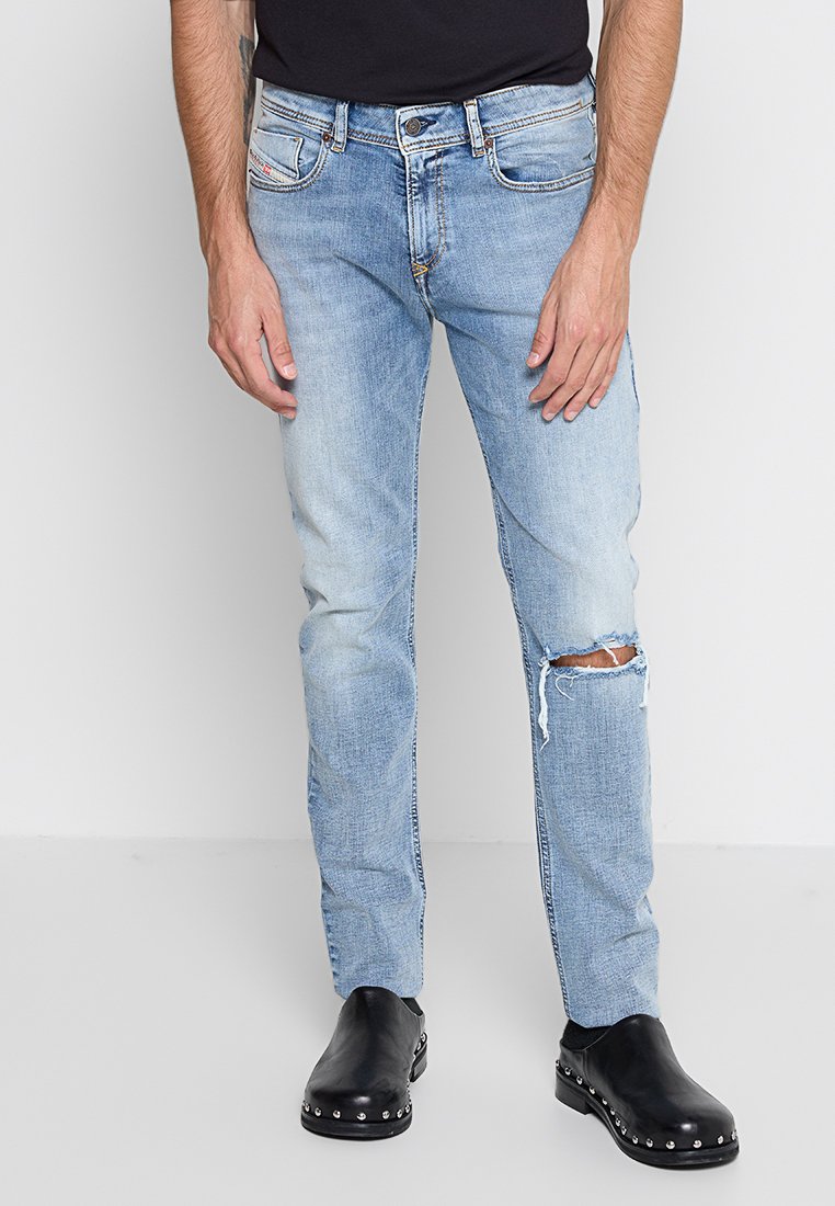 Helleblaue Denim-Jeans mit Slim-Fit, die ein distressed Knie und subtile Seitenschattierungen aufweisen, ergänzt durch ein klassisches Fünf-Taschen-Design.