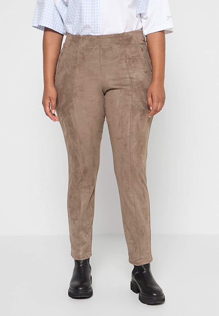 Braune, samtähnliche, enganliegende Hosen mit seitlichem Reißverschluss, taillierter Form und glatter Textur, kombiniert mit schwarzen Ankle-Boots.