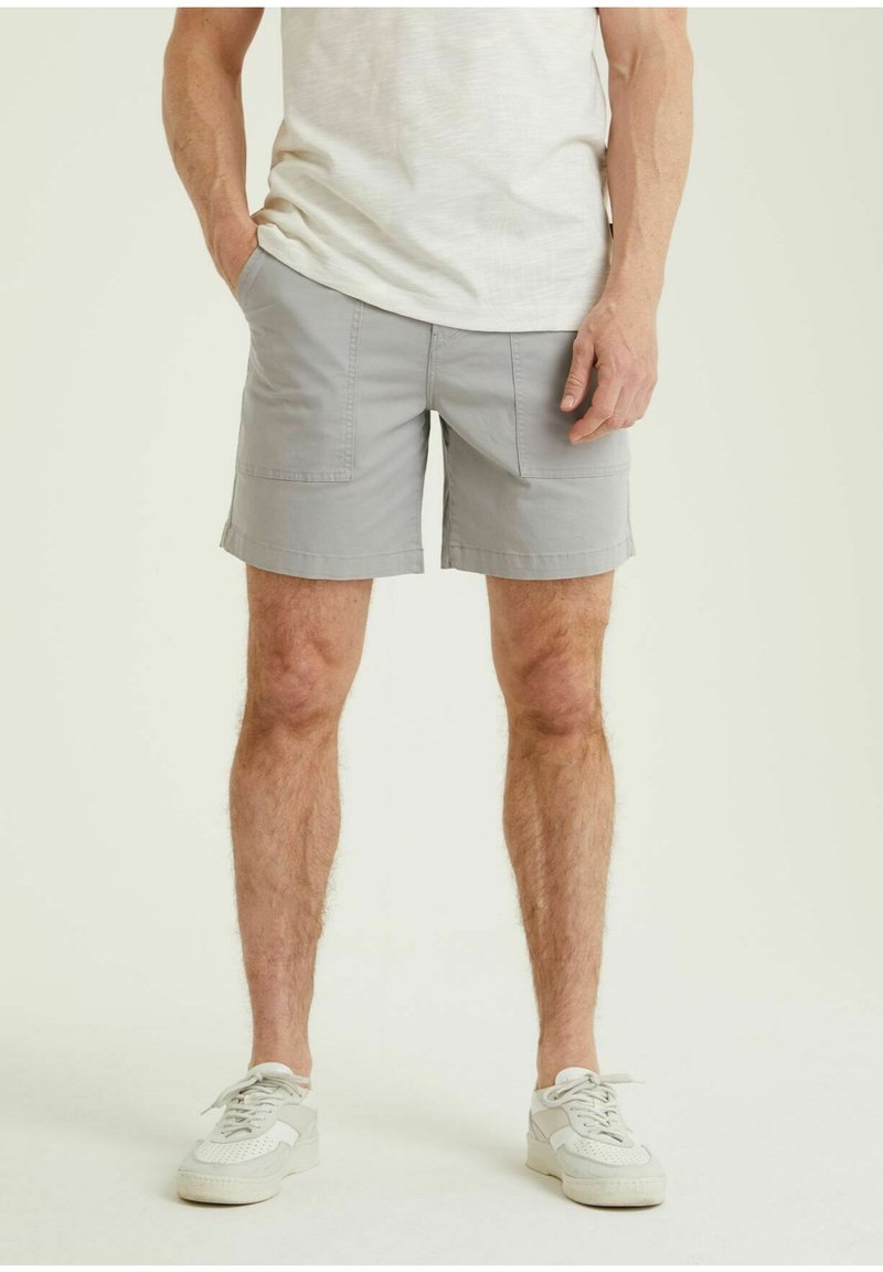 Graue Shorts mit zwei Fronttaschen, aus leichtem Stoff, mit geradem Schnitt und umgeschlagenem Saum. Kombiniert mit weißen Sneakern.