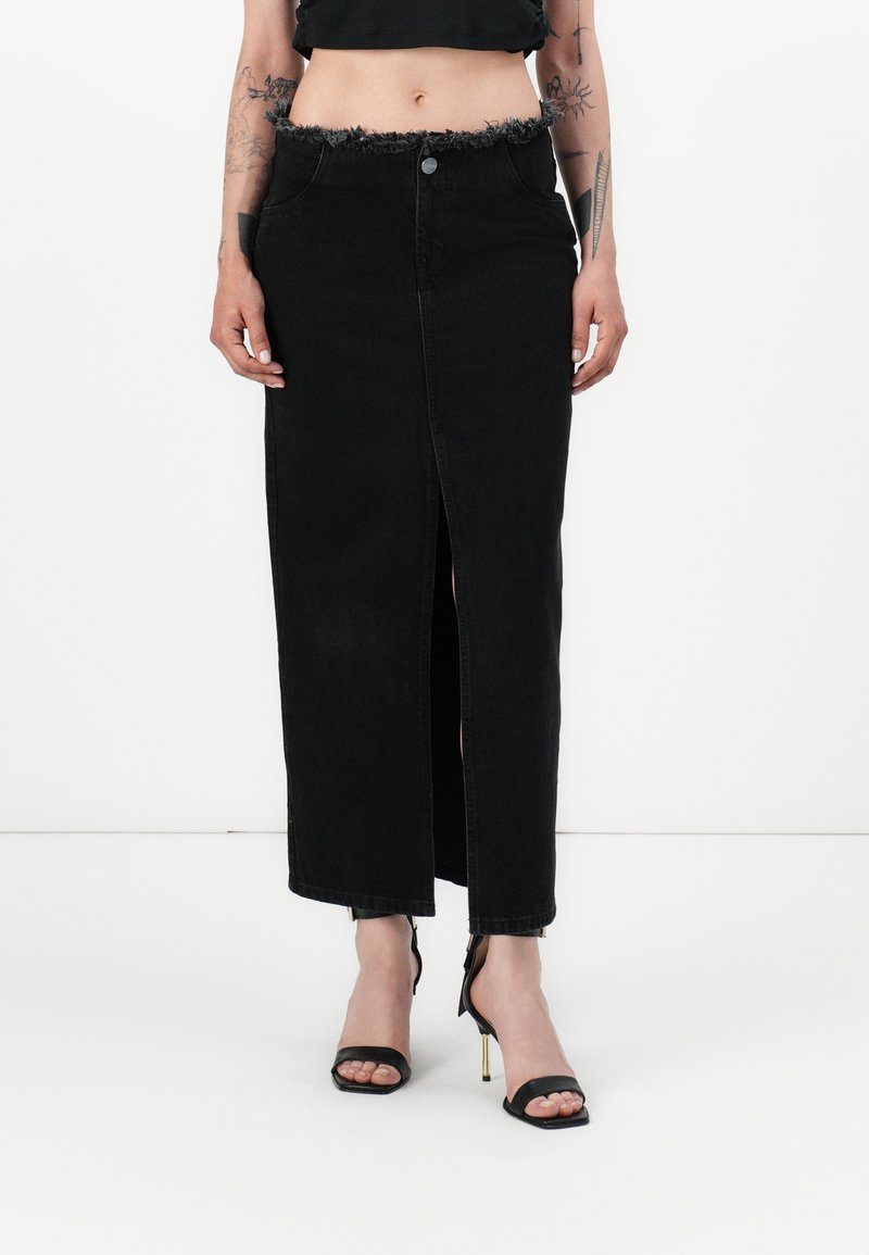 Schwarze Denim-Maxiröhre mit fransigem Taillenbund, vorderem Schlitz und klassischem Five-Pocket-Design, kombiniert mit schwarzen High-Heel-Sandalen.