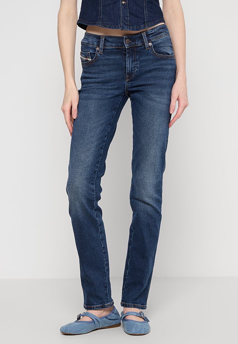 Dunkelblaue Denim-Jeans im Slim-Fit, mit genähten Taschen und einem leicht ausgewaschenen Look. Kombiniert mit hellblauen flachen Schuhen.