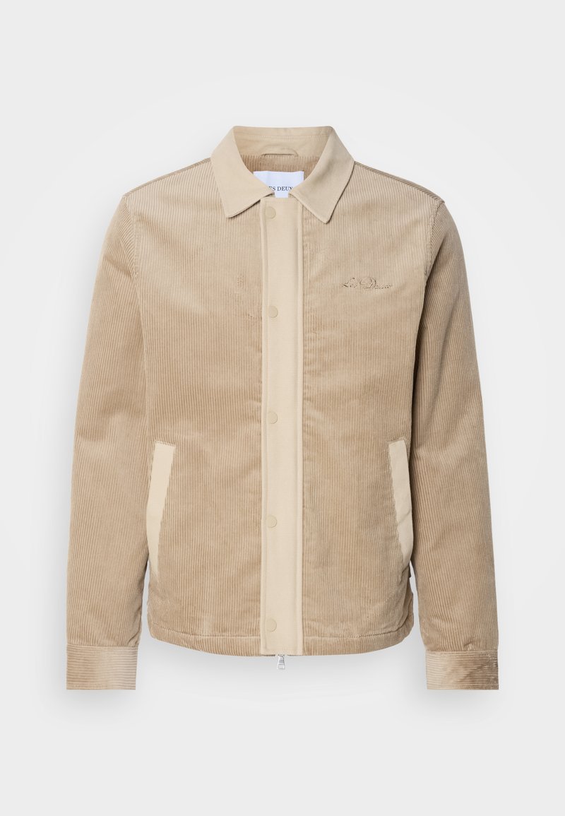 Beige Cordjacke aus Cord mit tanfarbenen Details an der Front, dem Kragen und den Taschen. Verfügt über eine Knopfverschluss und gerippte Bündchen. Subtile Markenkennzeichnung auf der Brust.