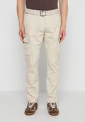 Mann trägt beige Cargohosen mit Seitentaschen, passenden Gürtel, braune Sneaker mit weißen Schnürsenkeln, steht vor einfarbigem Hintergrund.