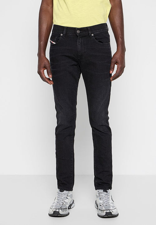 Schwarze Denim-Jeans mit schmalem Schnitt, Fünf-Taschen-Design, subtilen Nähtelementen und mittelhohem Bund, kombiniert mit grauen Sneakers.