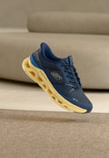 Marineblauer Skechers Sportschuh mit beiger, sechseckiger hohler Sohle, der über einem beigen Teppich in einem Raum mit neutralen Farbtönen schwebt.