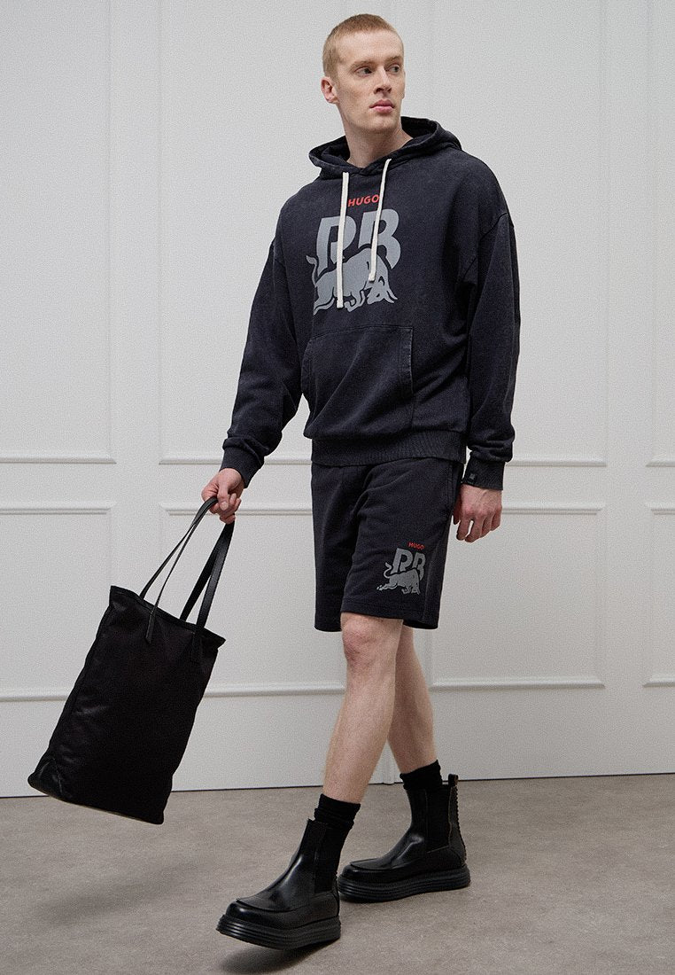 Dunkelgrauer Hoodie mit großem Grafikaufdruck, kombiniert mit passenden Shorts mit kleinem Logo. Schwarze Tragetasche und klobige schwarze Stiefel.