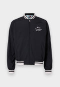 Schwarze Bomberjacke mit weißen Streifenakzenten an den Ärmelbündchen und dem Saum, versehen mit einem gestickten "NYC" und "Tommy Jeans est. 1985" Logo.