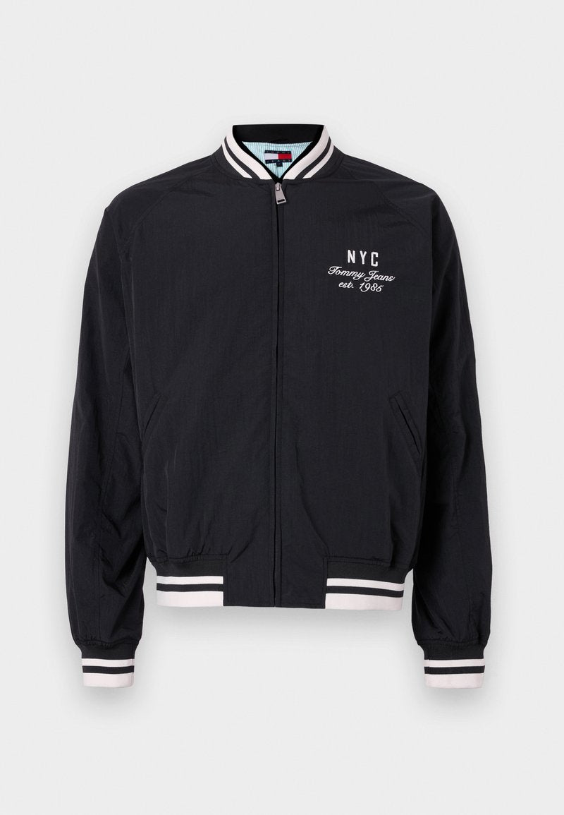 Schwarze Bomberjacke mit weißen Streifenakzenten an den Ärmelbündchen und dem Saum, versehen mit einem gestickten "NYC" und "Tommy Jeans est. 1985" Logo.