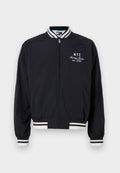 Schwarze Bomberjacke mit weißen Streifenakzenten an den Ärmelbündchen und dem Saum, versehen mit einem gestickten "NYC" und "Tommy Jeans est. 1985" Logo.