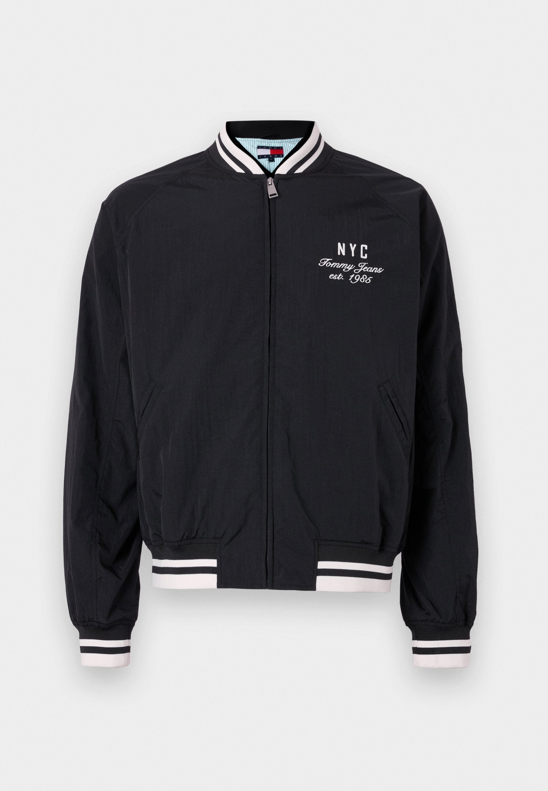 Schwarze Bomberjacke mit weißen Streifenakzenten an den Ärmelbündchen und dem Saum, versehen mit einem gestickten "NYC" und "Tommy Jeans est. 1985" Logo.