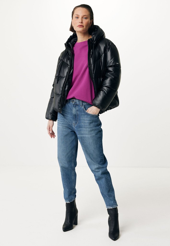 Schwarze Pufferjacke mit Kapuze, lila Pullover und blaue Jeans. Das Model trägt schwarze High Heels. Glatte Textur und lässige Passform.