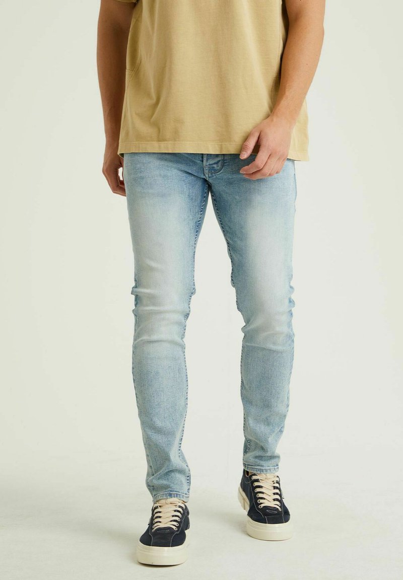 Helle blaue schmale Jeans aus Denim mit einer ausgewaschenen Optik, klassischem Fünf-Taschen-Design und subtilen Stickdetails, kombiniert mit dunklen Sneakern.