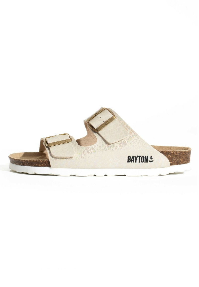 Beige Rutsch-Sandale mit zwei verstellbaren Riemen, die mit goldenen Schnallen versehen sind, einem strukturierten Obermaterial und einem Korkfußbett mit einer weißen Gummisohle.