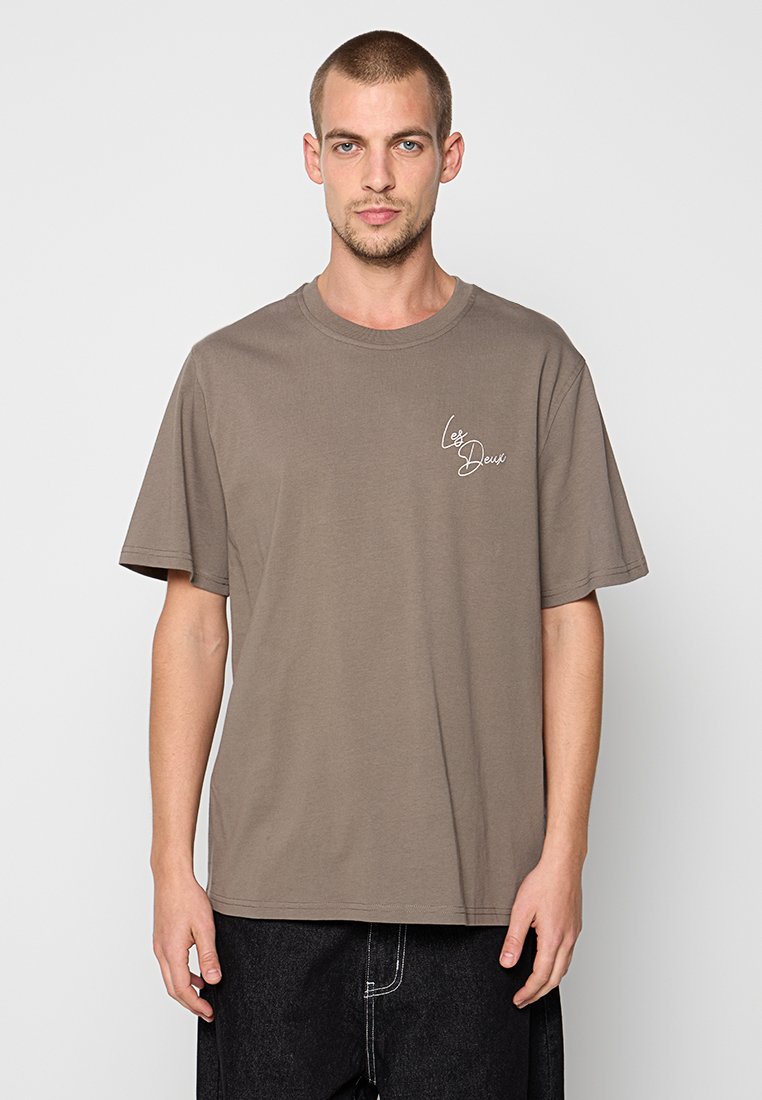 Braunes, kurzärmliges T-Shirt in lockerer Passform. Mit einem kleinen weißen Schriftlogo auf der linken Brust. Hergestellt aus weichem Baumwollmaterial.