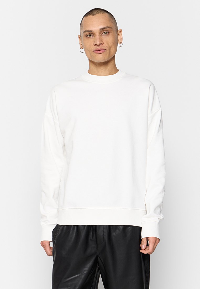 Weißes Sweatshirt mit Rundhalsausschnitt, langen Ärmeln und lässiger Passform, aus weichem Stoff; getragen über schwarzen Lederhosen.