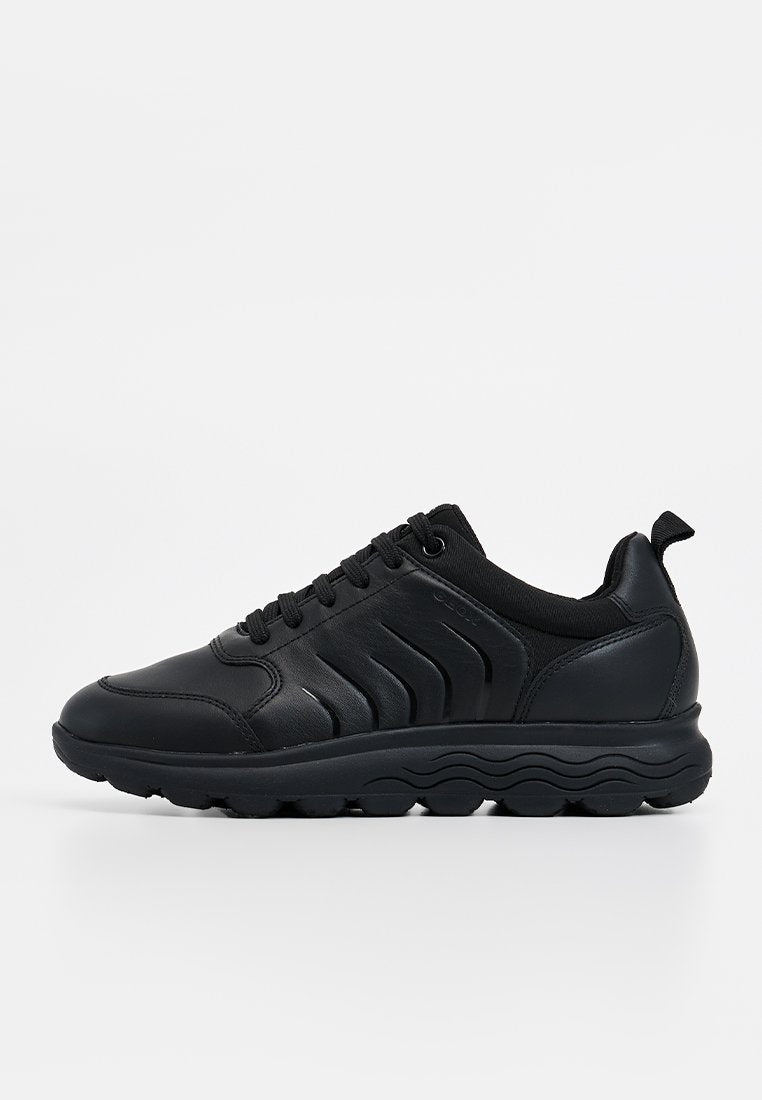 Schwarze Sportschuhe mit einem glatten Lederoberteil, strukturierten seitlichen Akzenten, gepolstertem Kragen und einer dicken Gummisohle.