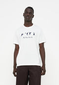Mann trägt ein weißes T-Shirt mit schwarzen abstrakten Figuren und dem Schriftzug „PS Paul Smith“, kombiniert mit dunkelbrauner Hose, steht vor weißem Hintergrund.