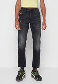Person, die verblasste schwarze Jeans mit Used-Effekten, schwarze Sneakers mit neongrünen Schnürsenkeln und ein hellgelbes Crop-Top trägt, steht vor einem weißen Hintergrund.