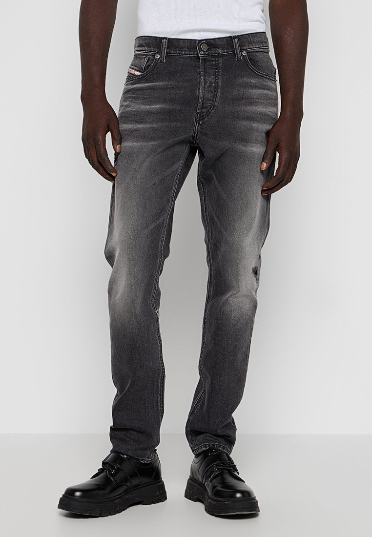 Graue Jeans aus Denim mit einem ausgewaschenen Finish, geradem Schnitt, fünf Taschen Design und einem kleinen Logo-Detail auf der vorderen Tasche. Getragen mit schwarzen Schuhen.