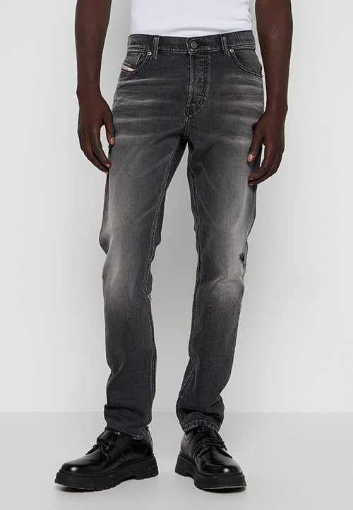 Graue Jeans aus Denim mit einem ausgewaschenen Finish, geradem Schnitt, fünf Taschen Design und einem kleinen Logo-Detail auf der vorderen Tasche. Getragen mit schwarzen Schuhen.
