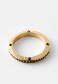 Goldener Armreif mit eingraviertem "GUESS"-Schriftzug, versehen mit schwarzen Akzenten und Steinen rund um das Band. Glatte Textur und rundes Design.