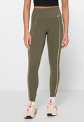 Olivgrüne Leggings mit hoher Taille aus elastischem Stoff, mit goldfarbenen Seitenstreifen und kleinem weißem Logo. Kombiniert mit hellen Sneakern.
