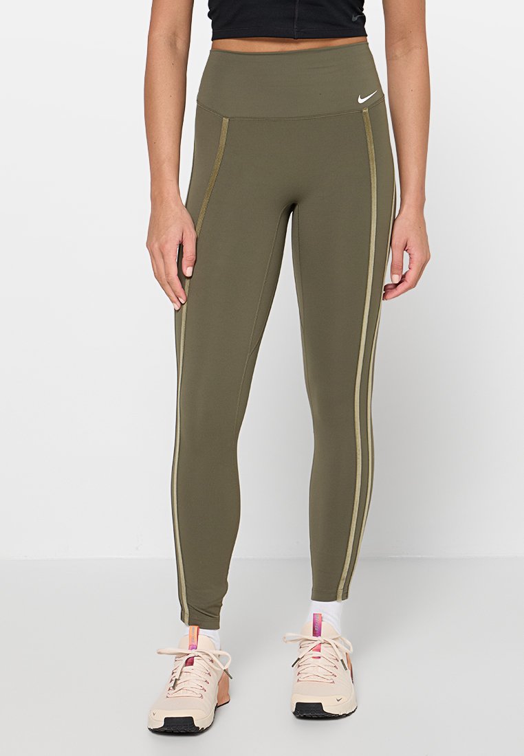 Olivgrüne Leggings mit hoher Taille aus elastischem Stoff, mit goldfarbenen Seitenstreifen und kleinem weißem Logo. Kombiniert mit hellen Sneakern.