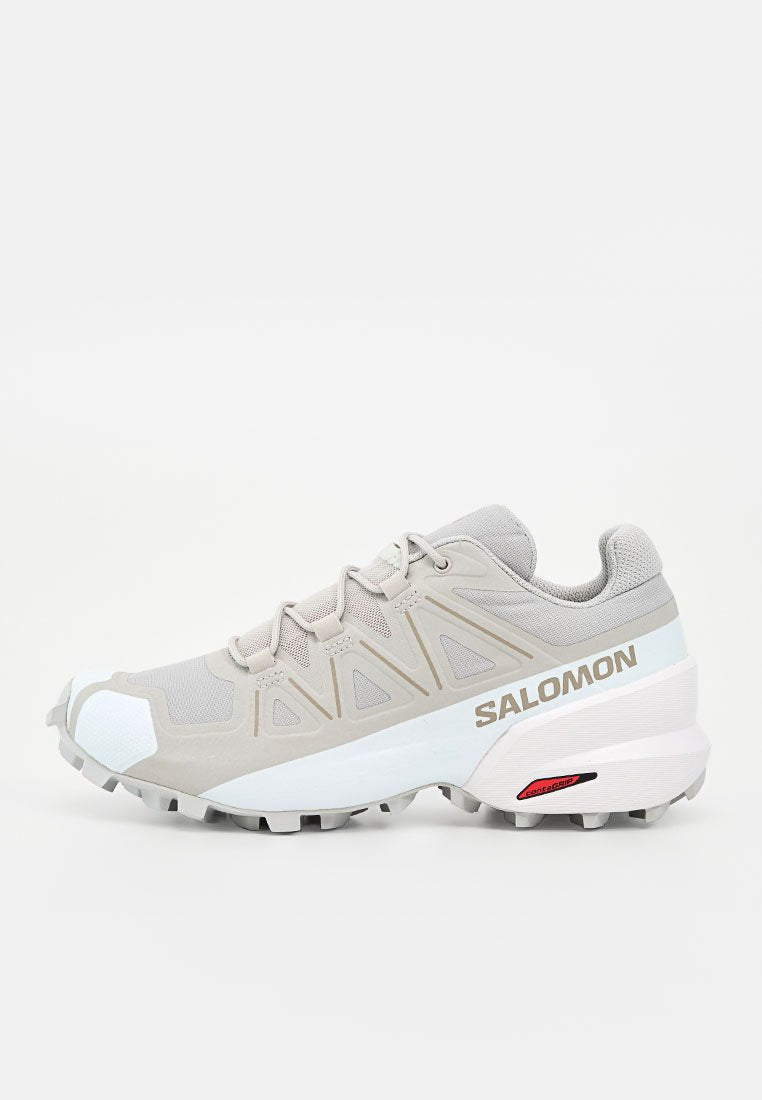 Hellgrauer und weißer Salomon Trailrunning-Schuh mit robustem Profil und gebrandetem Seitenpanel, dargestellt von der Außenseite.