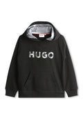 Schwarzer Hoodie aus weichem Stoff mit einer Fronttasche. Verfügt über ein graues Innenfutter und ein großes, silbernes "HUGO"-Logo über der Brust.
