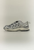Hellgrauer Salomon Trailrunning-Schuh mit Mesh-Einsätzen, Schnellbändersystem und robuster schwarzer Sohle, seitlich auf neutralem Hintergrund gezeigt.