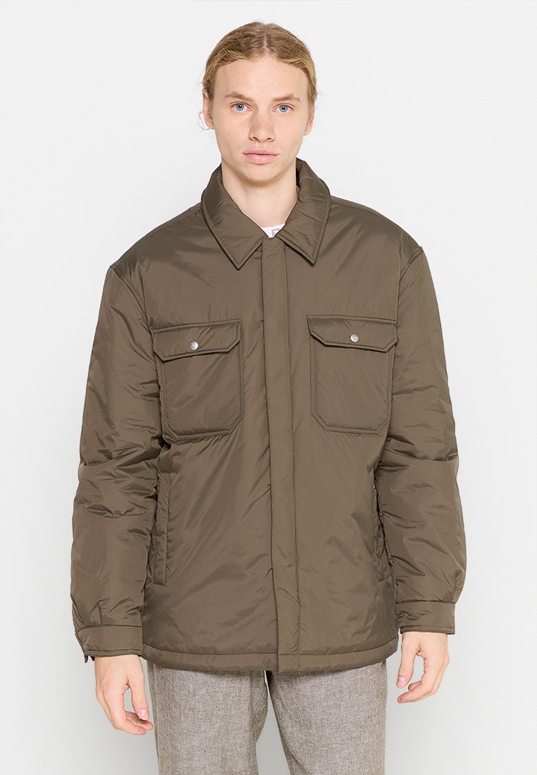 Olivgrüne, isolierteJacke mit Kragen, zwei Brusttaschen und einem vorderen Druckverschluss. Weicher, gesteppten Textur mit elastischen Bündchen.