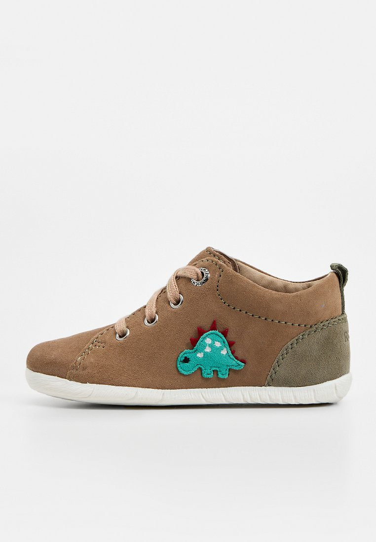 Brauner Wildleder-Toddler-Schuh mit beigen Schnürsenkeln und einem grünen Dinosaurier-Patch an der Seite, ausgestattet mit einer weißen flexiblen Sohle und einem olivgrünen Fersendetail.