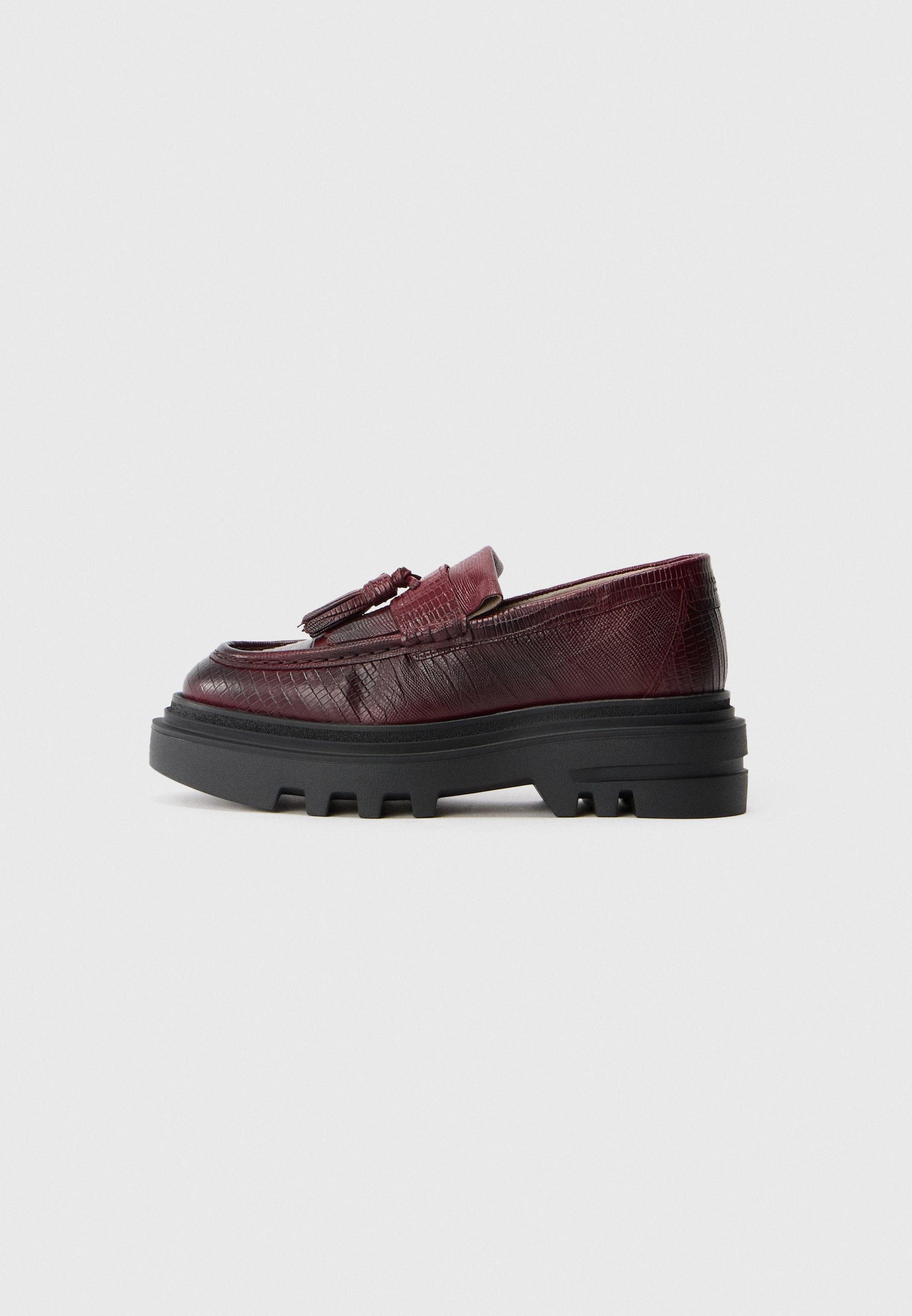 Burgunderfarbene Lederloafer mit strukturiertem Finish, ausgestattet mit einer klobigen schwarzen Sohle und einem kleinen Quastenakzent auf der Vorderseite.