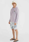 Lila Kapuzenpullover mit Fronttasche und Logopatch, kombiniert mit gemusterten pastellfarbenen Badeshorts mit Blattdesigns. Schwarze Flip-Flops runden das Outfit ab.