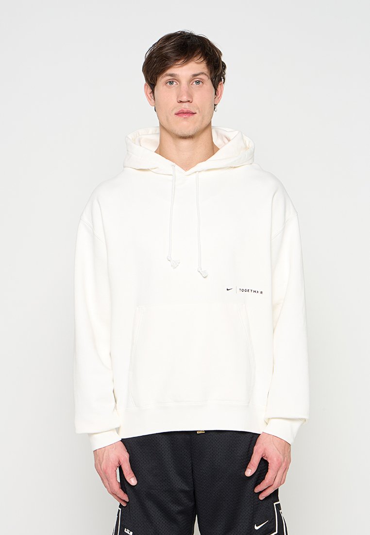 Junger Mann trägt einen weißen Nike-Hoodie mit dem Schriftzug "TOGETHER" und schwarze Nike-Shorts, steht vor einem schlichten hellen Hintergrund.