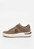 Brauner Wildleder-Niedrigschnitt-Sneaker mit weißer Sohle, rundem Metall-Logo an der Seite und Schnürverschluss auf neutralem Hintergrund.