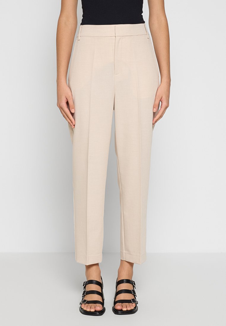 Beige maßgeschneiderte Hose mit hoher Taille, gefaltetem Frontbereich und geradem Bein. Glatter Stoff in neutraler Farbe für vielseitige Styling-Optionen. Schwarze Riemchensandalen.