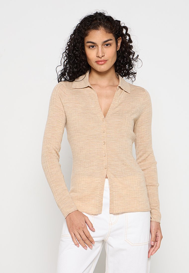 Beige Langarm-Hemd mit Knopfleiste, kragenförmigem Ausschnitt, strukturiertem Stoff und figurnahem Schnitt, kombiniert mit weißen Hosen.