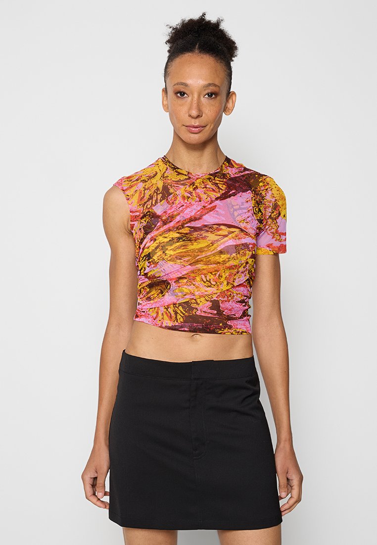 Kurzes, ärmelloses Oberteil in lebhaftem Pink mit gelben und braunen abstrahierten Mustern; glatte Textur mit tailliertem Design, kombiniert mit einem schwarzen Rock.