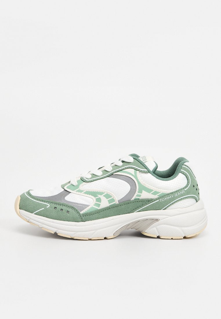 Weißer und grüner Sportschuh mit dicker Sohle, wellenförmigem Design, Schnürverschluss und "Tommy Jeans"-Markierung an der Ferse.